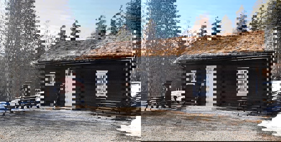 Bild som visar bagarstugan, taget på vårvinter med lite snö kvar på marken. Stugan är röd med vit dörr och vita fönster. Tegelpannor på taget.